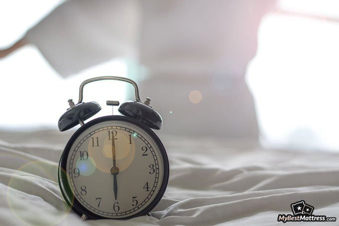 How to fix sleep schedule: a clock in front of a woman waking up in the morning