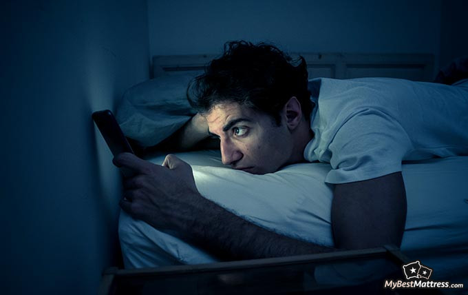 Coronavirus sleep: a man browsing his phone in bed. Coronavirus sleep: a man browsing his phone in bed.