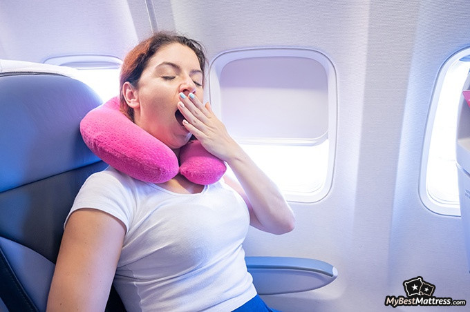 How To Sleep On A Plane: a woman yawning on a plane.