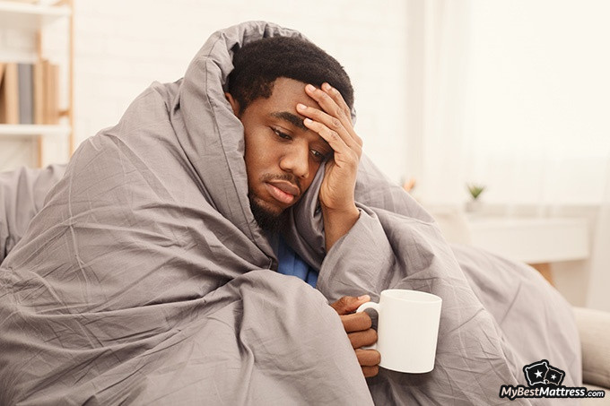 How To Sleep With A Cold: sick man bundled up in a warm blanket.