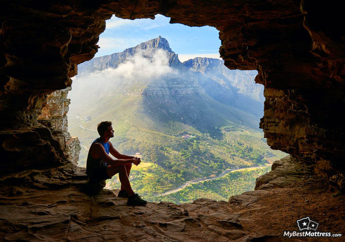 Hypnosis For Sleep: man sitting in a cave with a nice view.