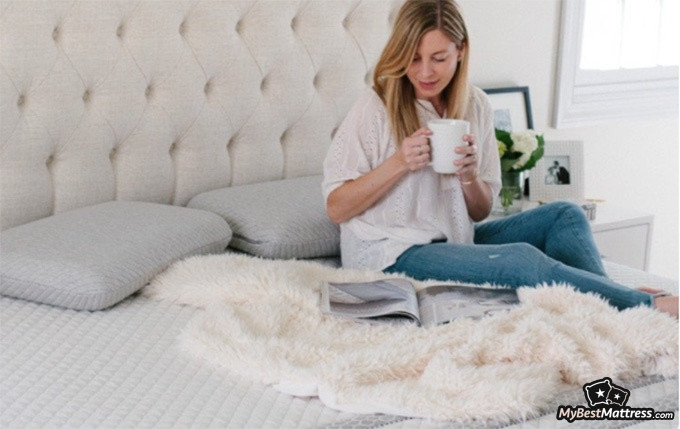 Leesa Hybrid Mattress Review: woman sitting on a leesa mattress. Leesa Hybrid Mattress Review: woman sitting on a leesa mattress.