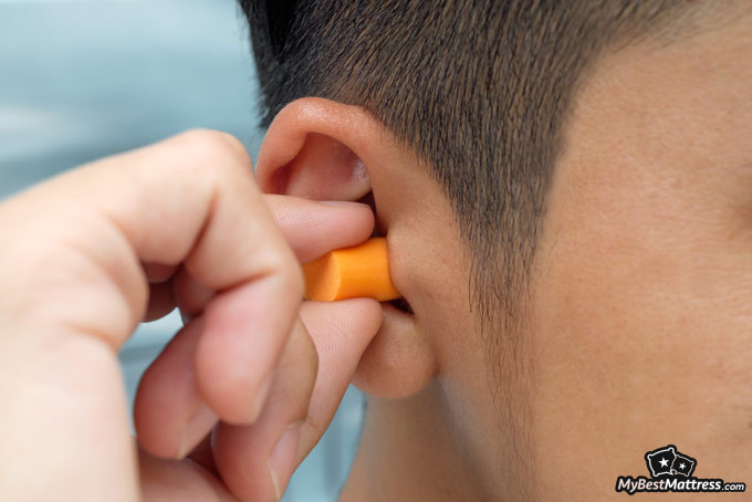 Best earplugs for sleeping: man putting earplugs into his ears.