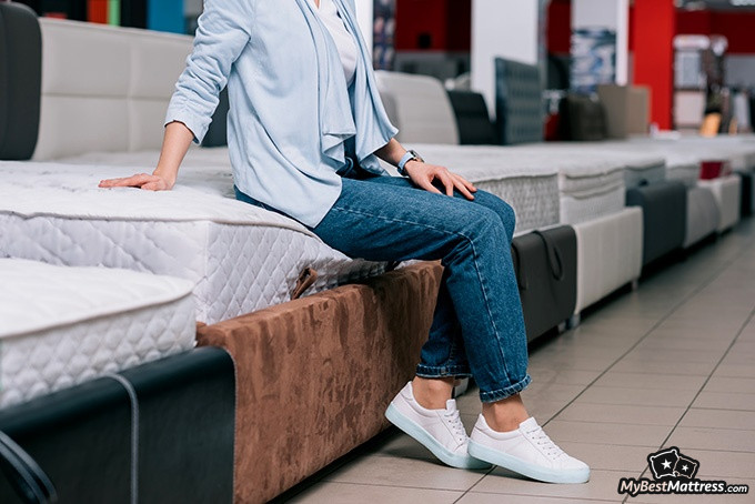 Sealy Posturepedic mattress reviews: a woman is sitting on a mattress in a mattress shop Sealy Posturepedic mattress reviews: a woman is sitting on a mattress in a mattress shop